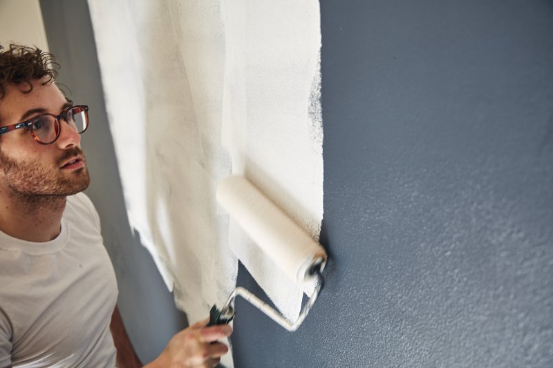 Man applying primer to a dark wall (Photo by EyeWolf / Moment via Getty Images)